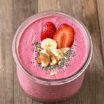Close-up of a freshly blended Hailey Bieber smoothie in a clear glass jar, featuring a creamy pink color from strawberries and banana.